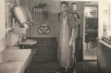 Patriarch, Jack Appel, milking apron on, standing in the milk house. 